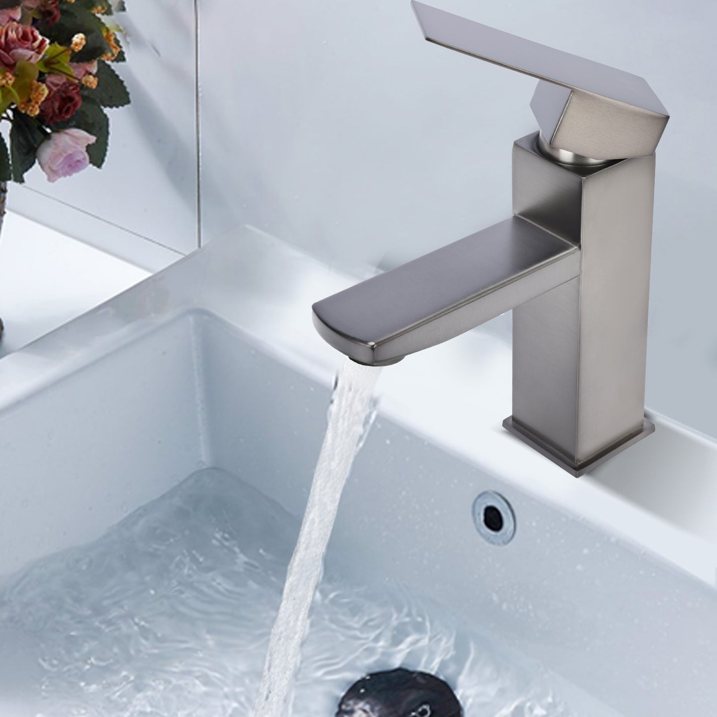 Modern silver faucet with water flowing into a sink, with flowers in the background.