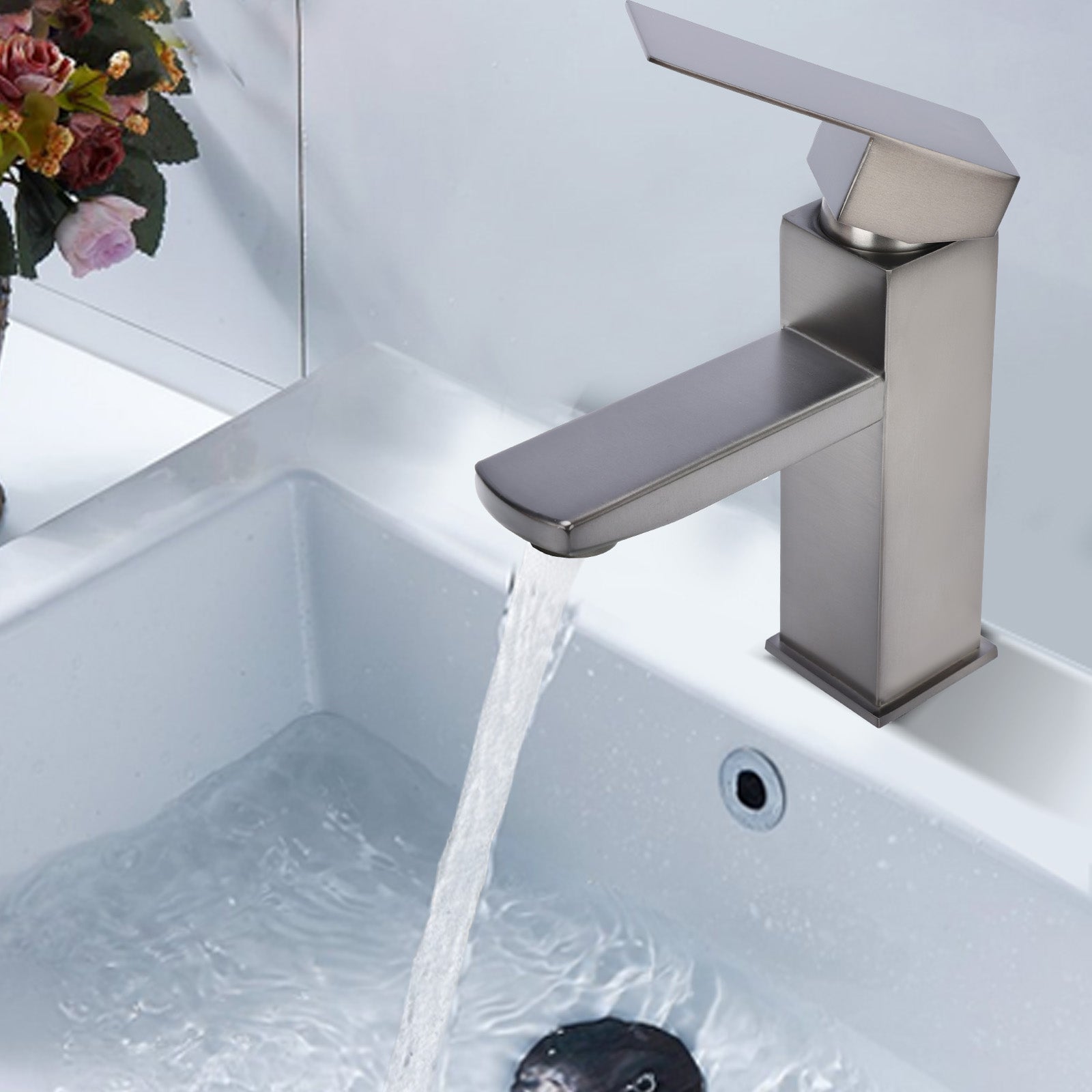 Modern silver faucet with water flowing into a sink, with flowers in the background.