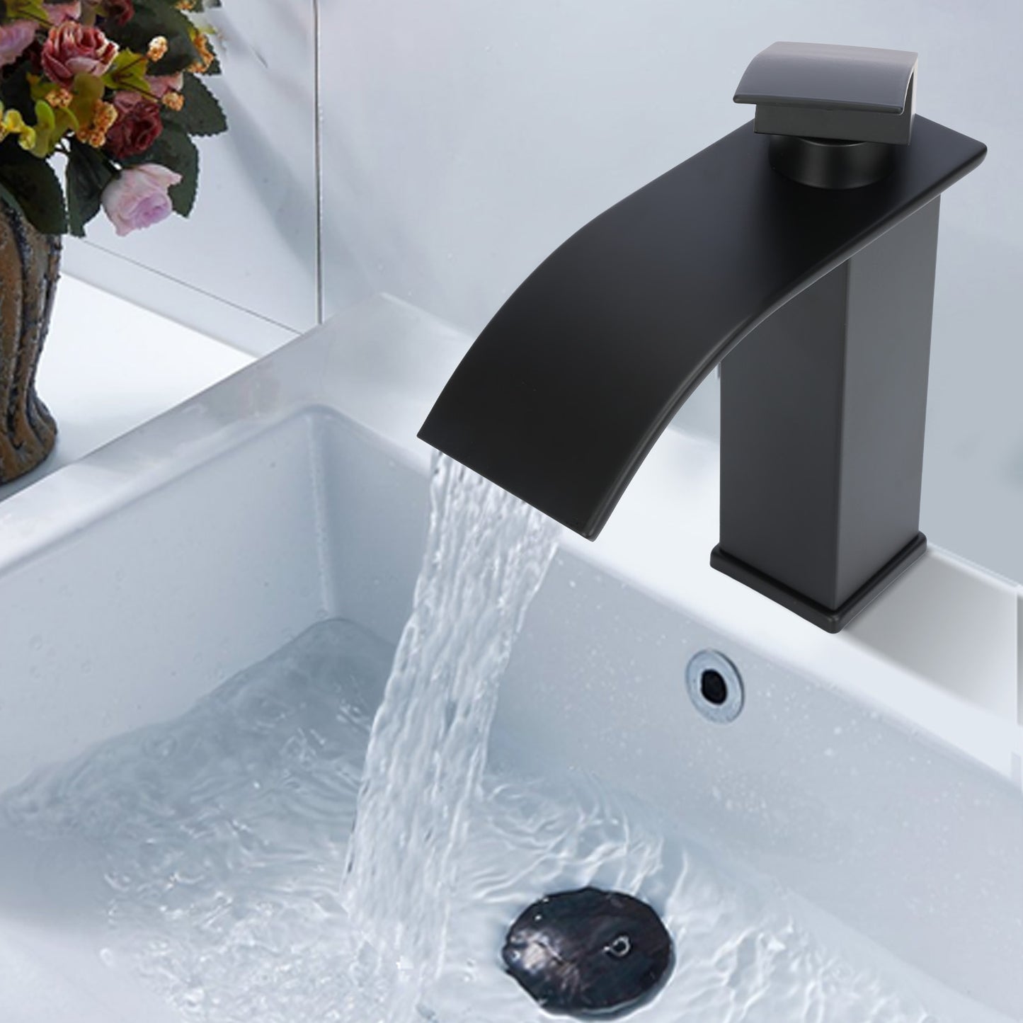 Black faucet with water flowing into a sink, with flowers in the background.