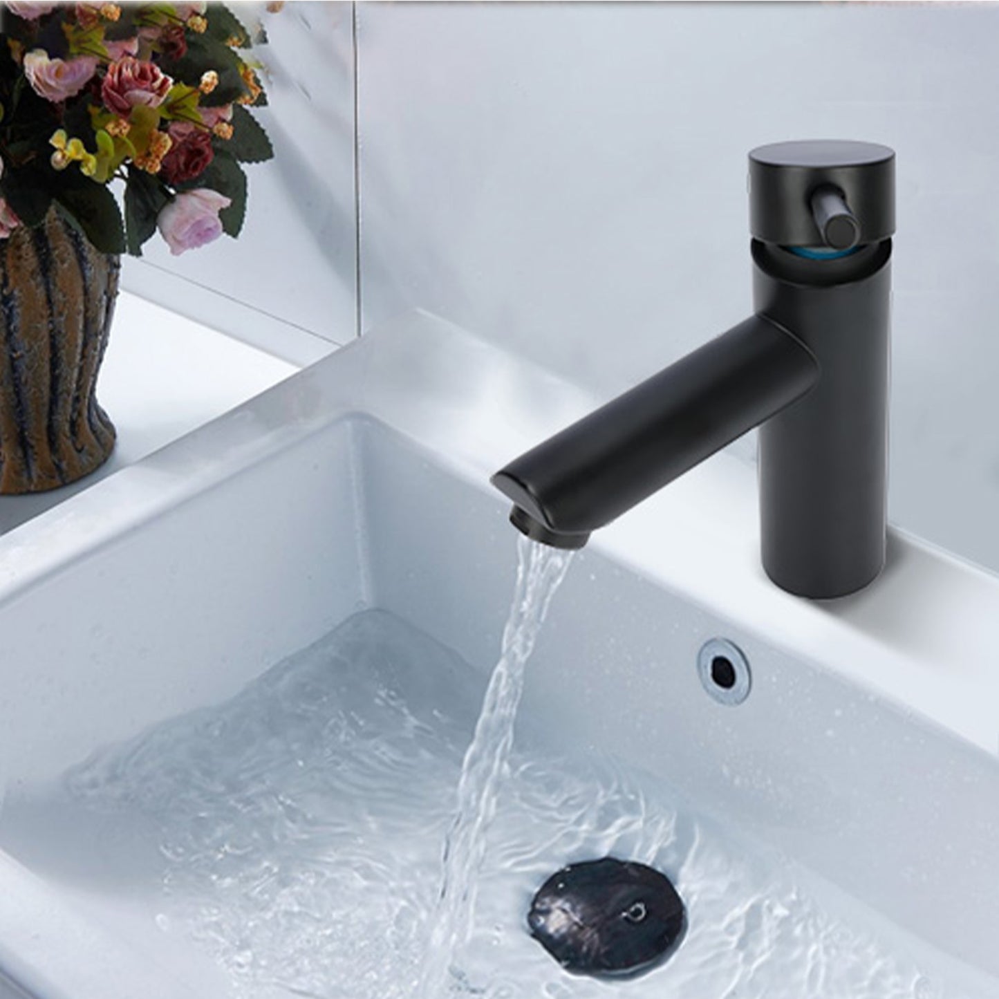 Black faucet with water flowing into a sink, with flowers in the background.
