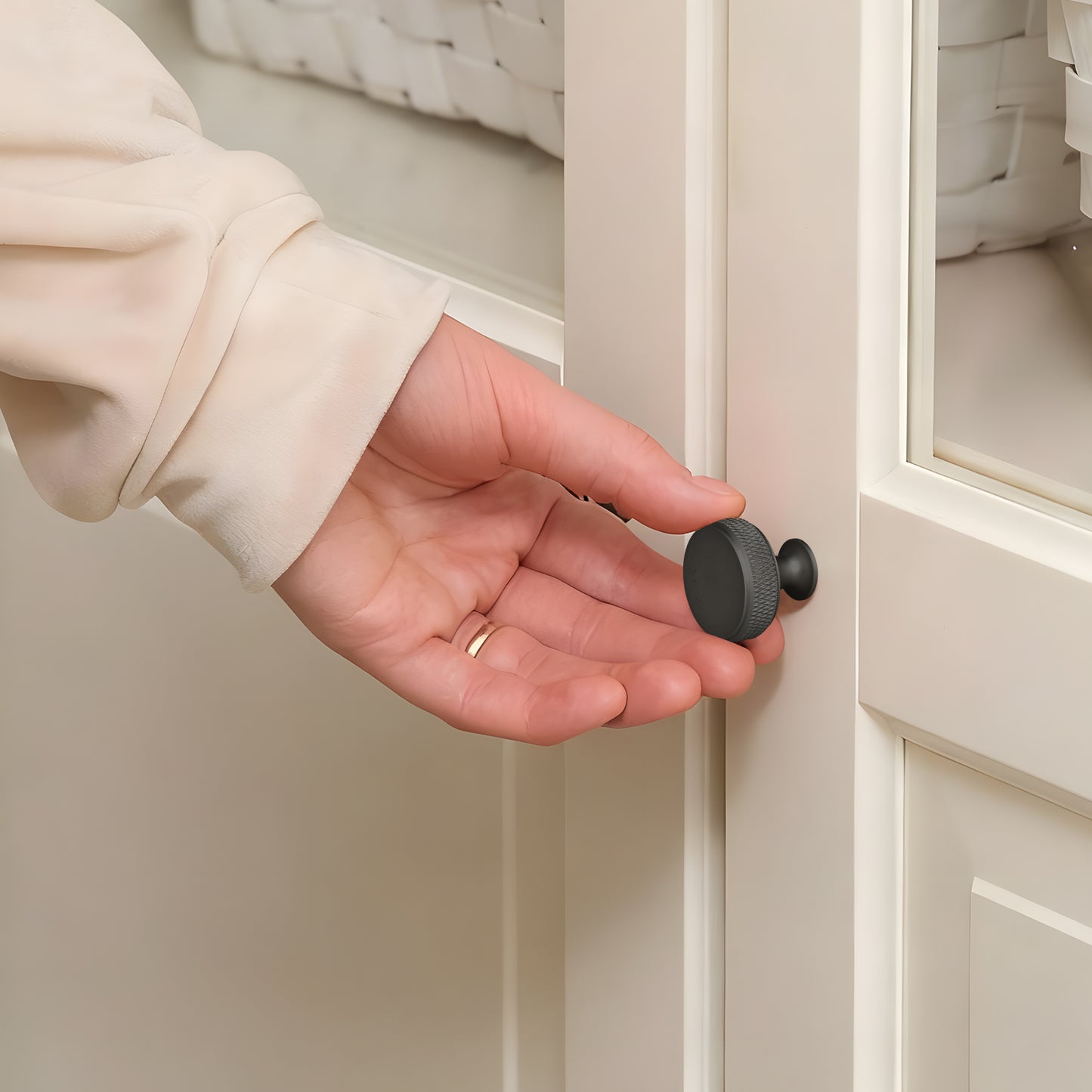 Hand holding a black cabinet knob in front of a beige cabinet.