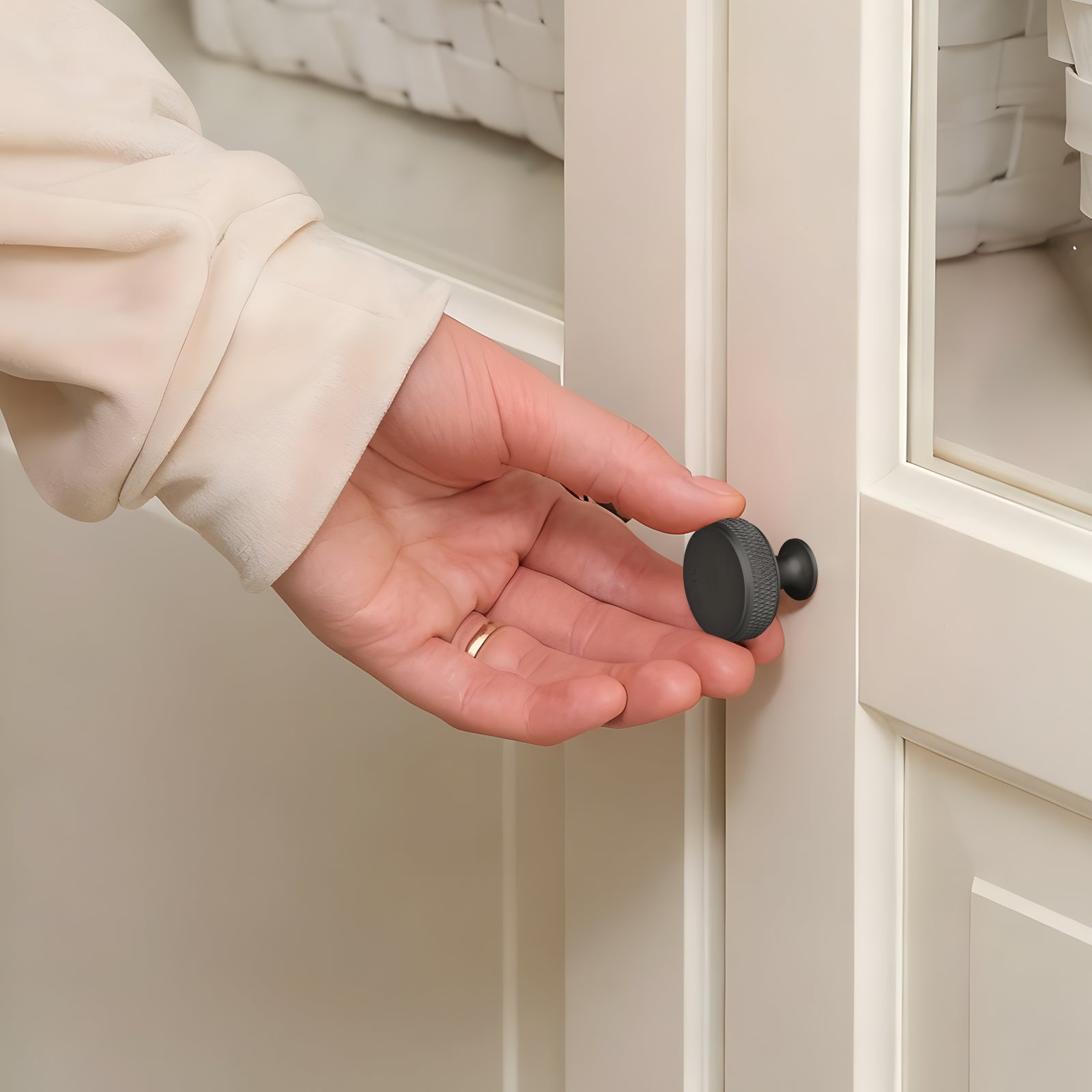 Hand holding a black cabinet knob in front of a beige cabinet.