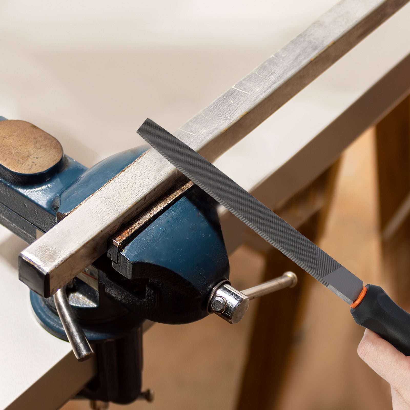 Person using a file on a metal bar clamped in a vise.