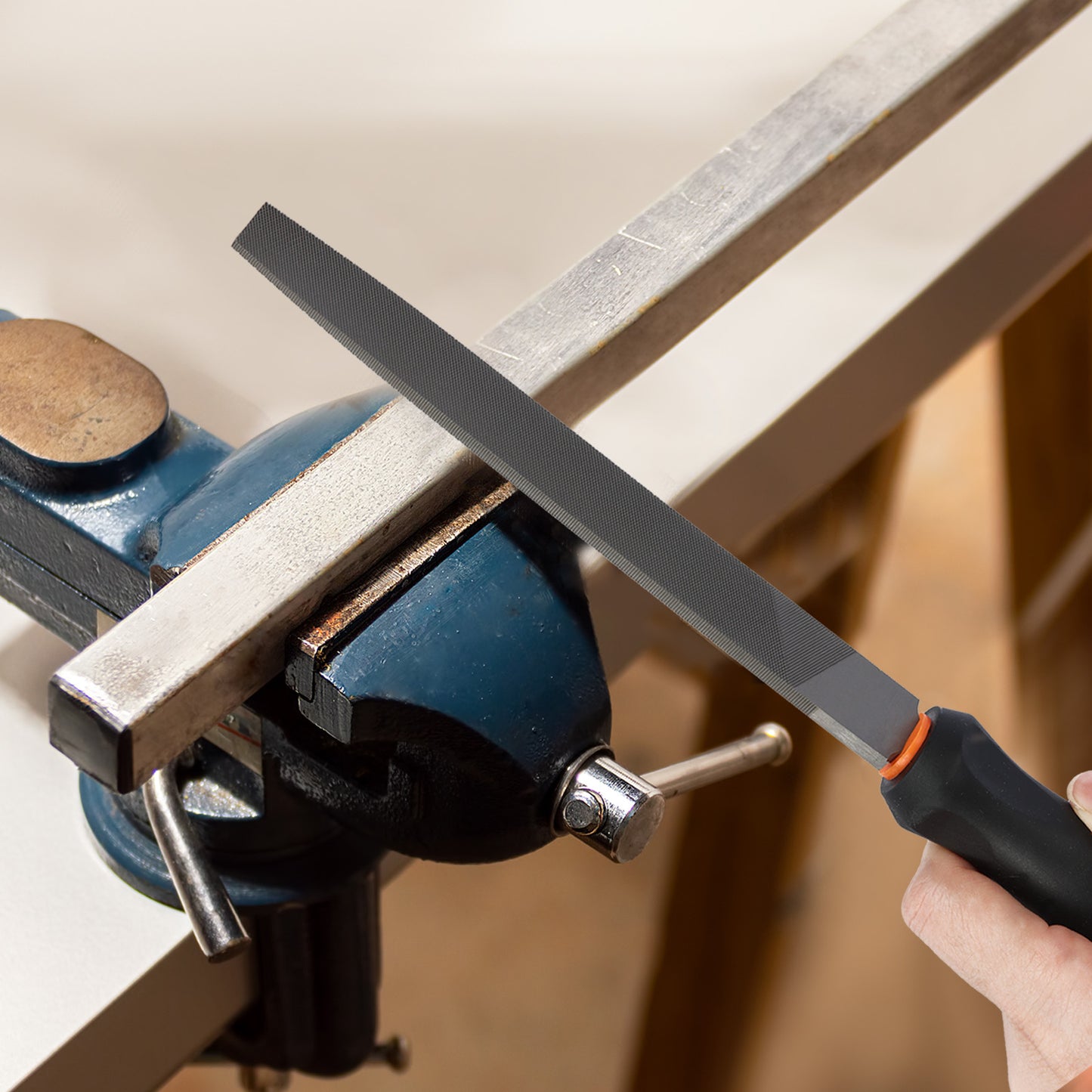 Person using a file on a metal bar clamped in a vise.