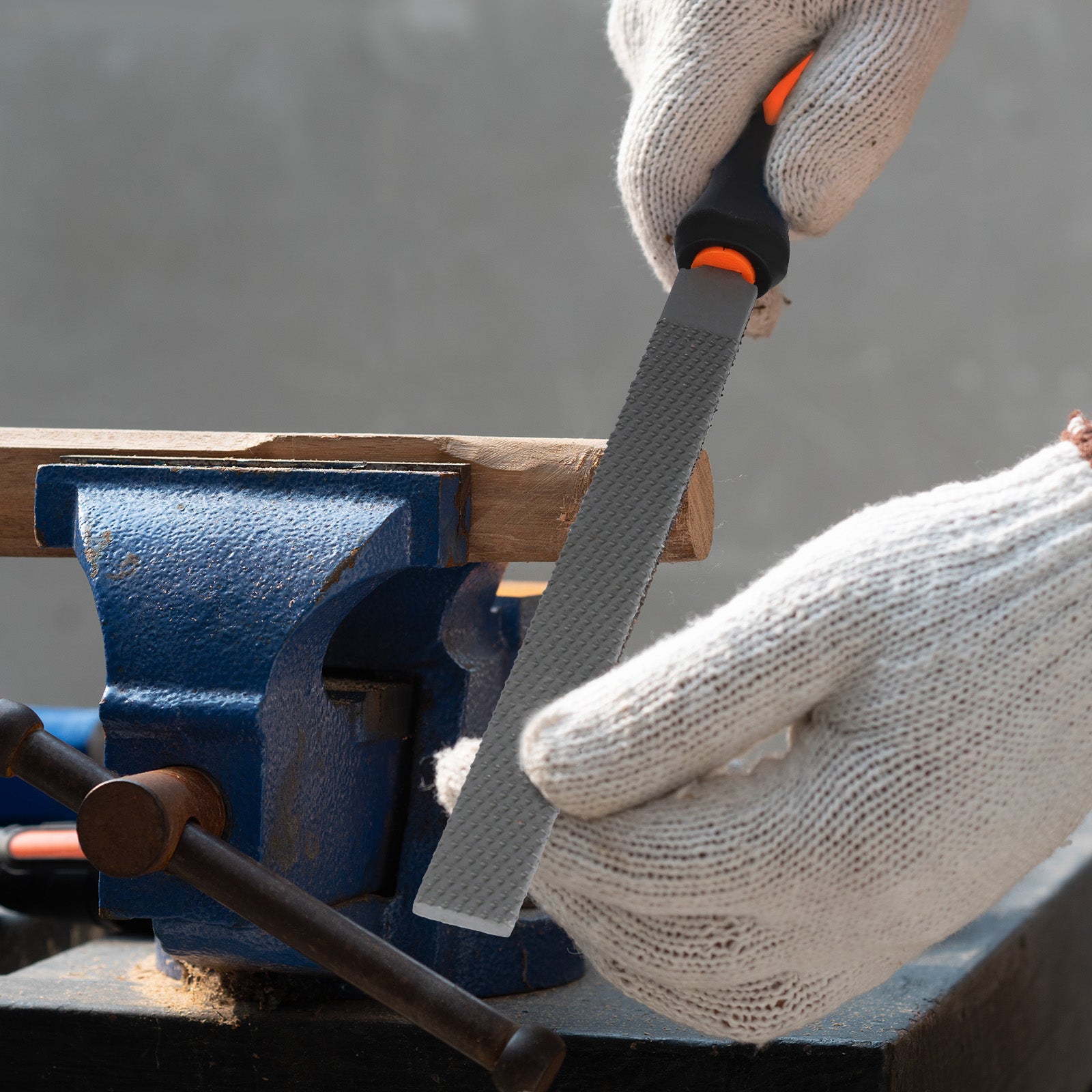 Person wearing gloves using a file on a piece of wood held in a blue vise.