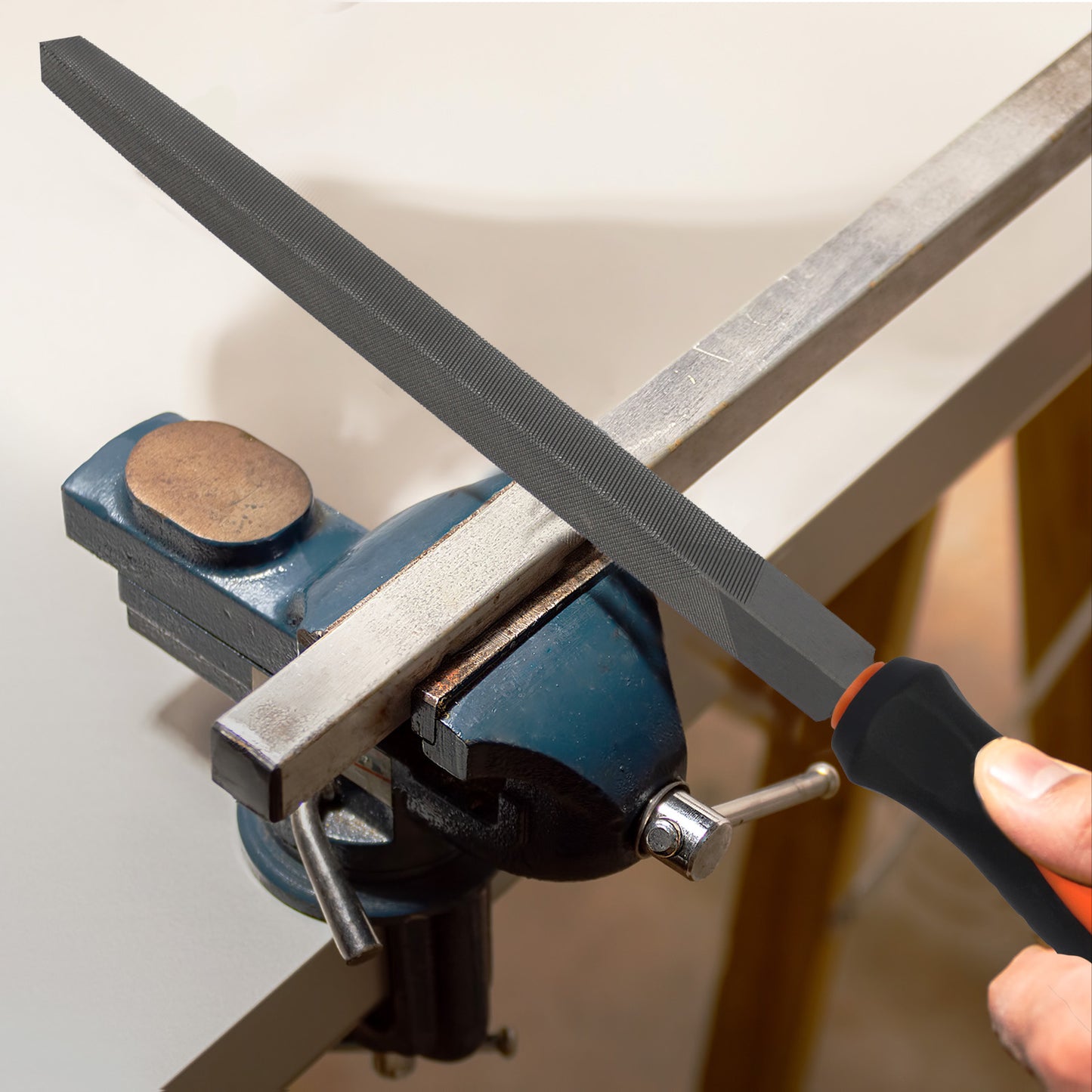 Person using a file on a metal bar clamped in a vise.