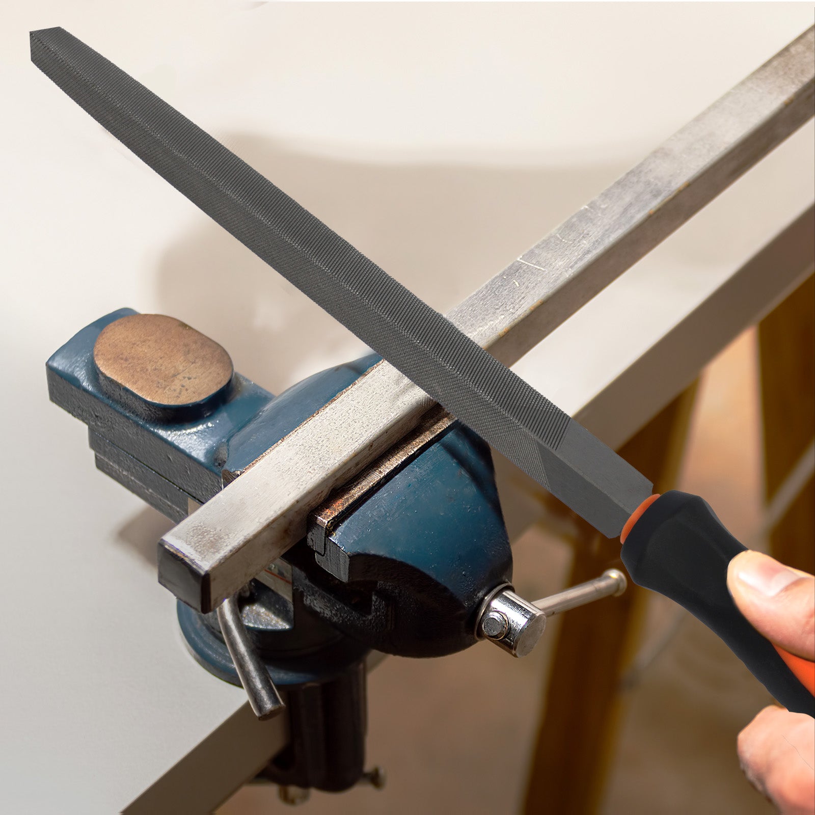 Person using a file on a metal bar clamped in a vise.