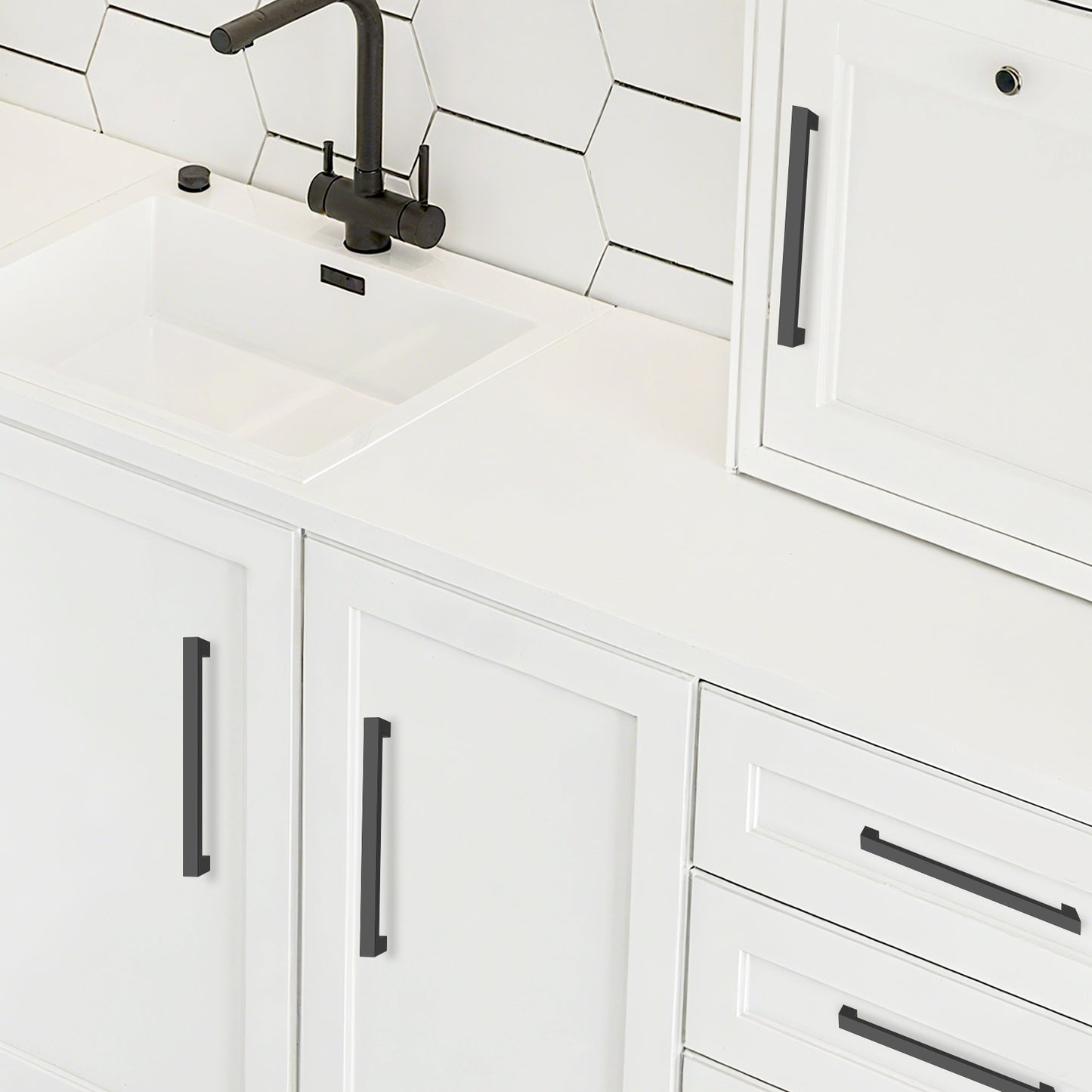 White kitchen cabinets with black handles and a tiled backsplash.