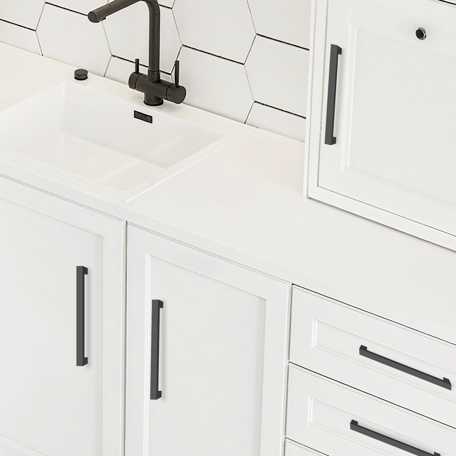 White kitchen cabinets with black handles and a tiled backsplash.