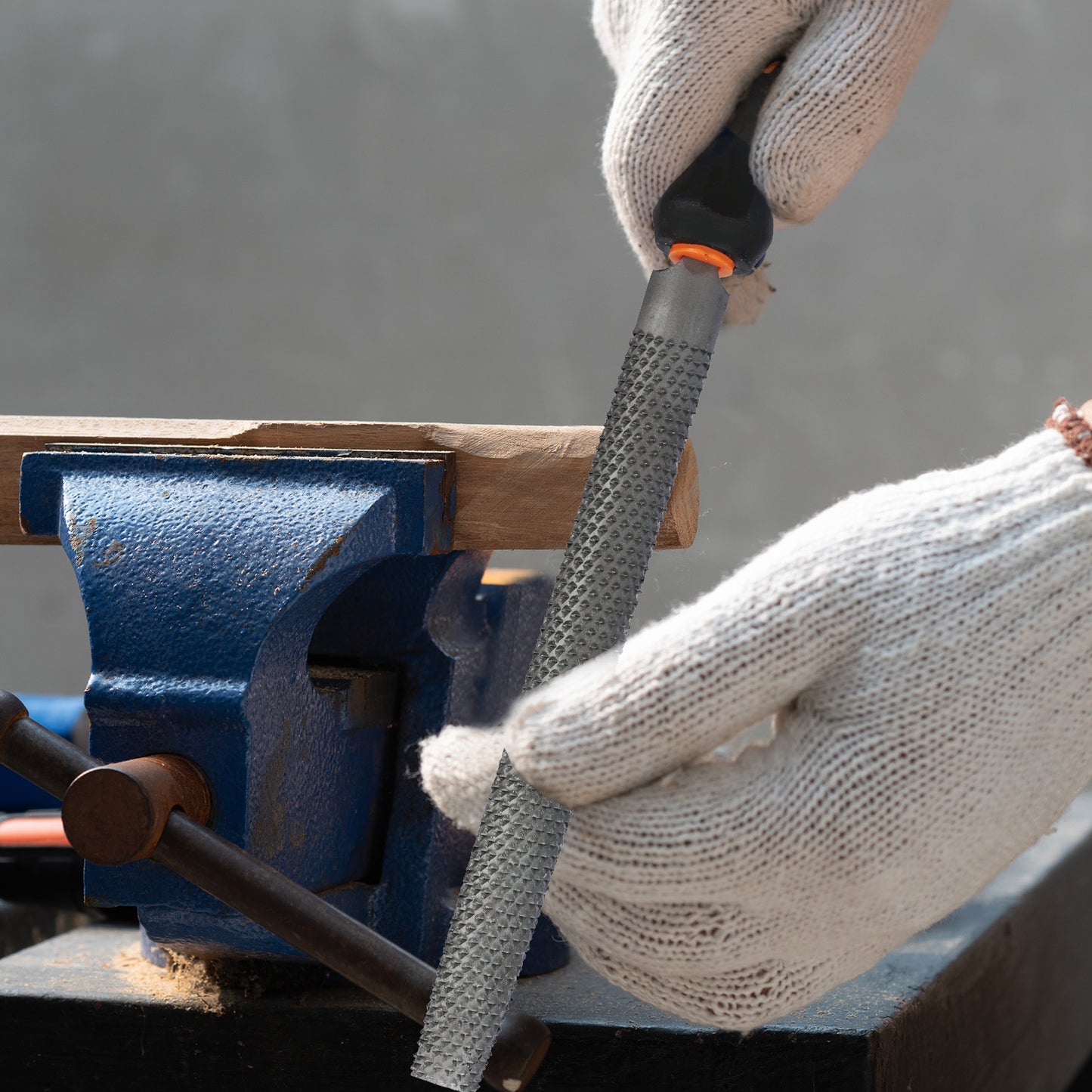 Person using a blue vise with a wooden block and metal tool on a gray background