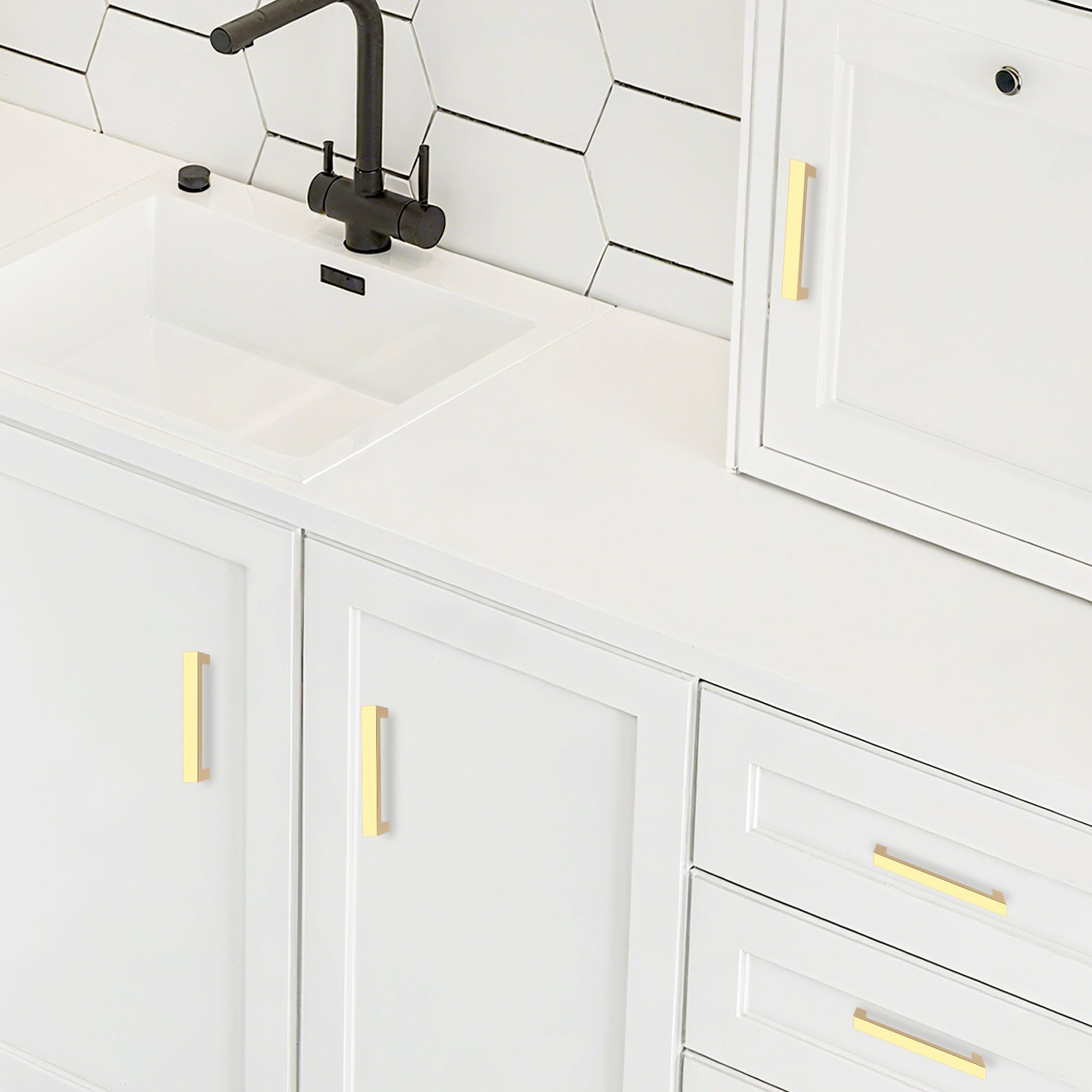 White kitchen cabinets with gold handles and a black faucet.