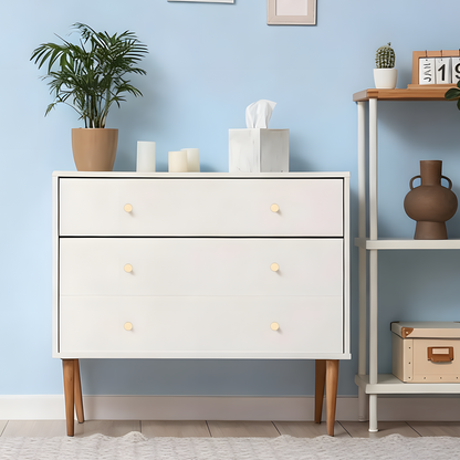 White dresser with wooden legs against a light blue wall with decorative items.