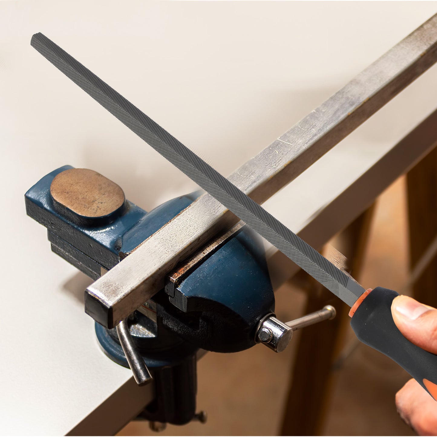 Person using a file on a metal bar clamped in a vise.