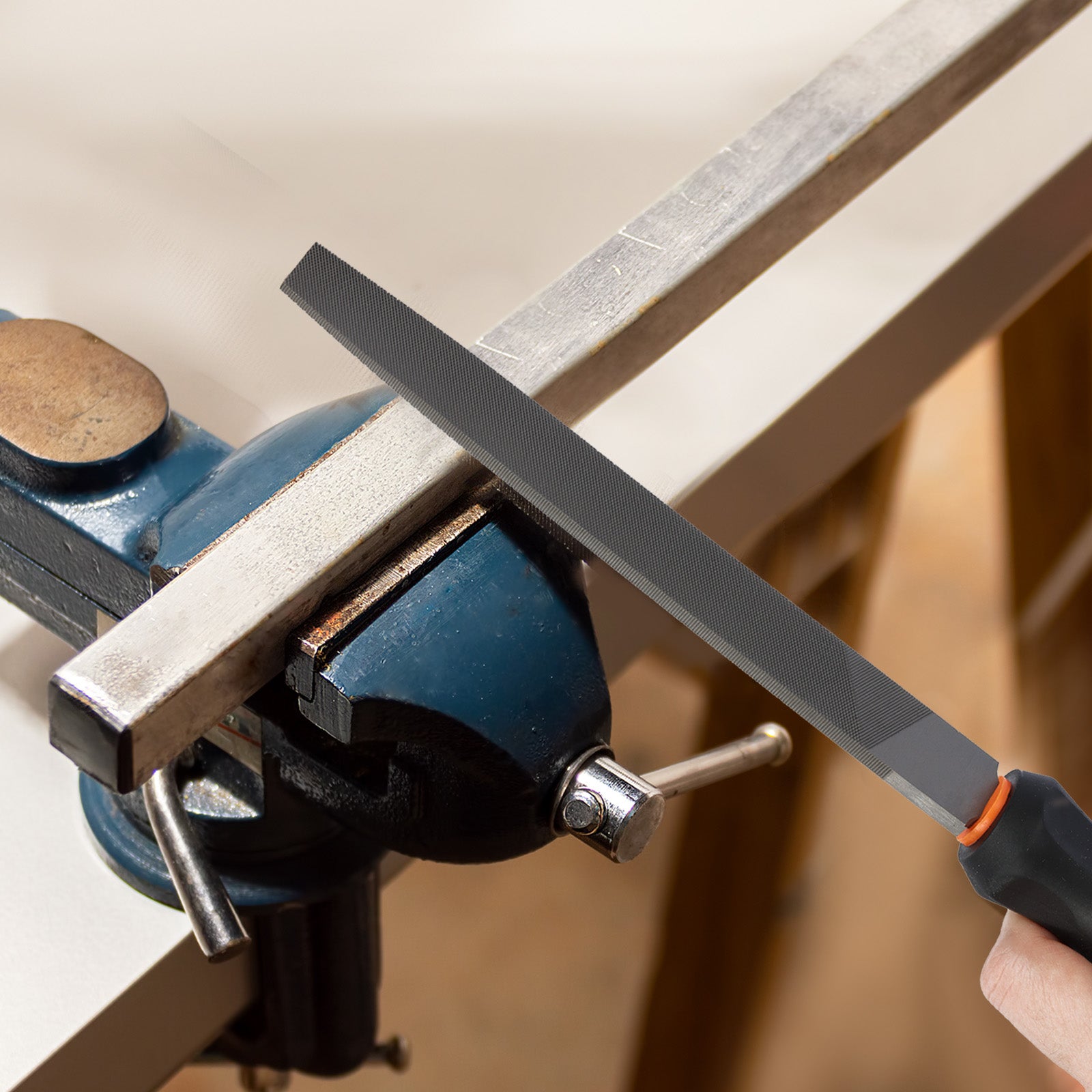 Person using a file to sharpen a metal bar clamped in a vise.