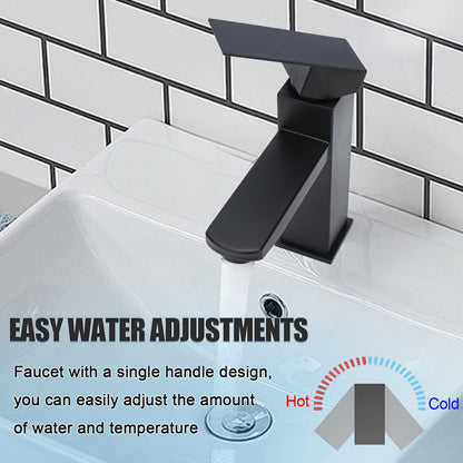Black faucet on a sink with water flowing, against a tiled bathroom wall.